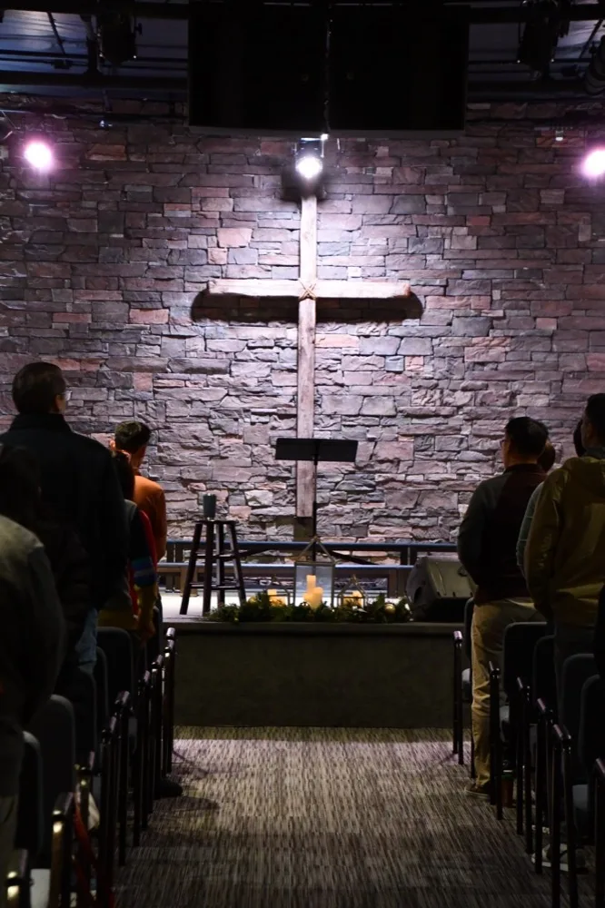 The congregation standing before the wooden cross on the stone wall of the Lighthouse sanctuary
